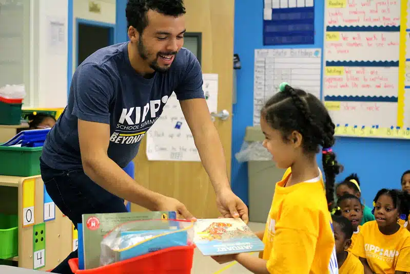 Teacher giving a book to a child.